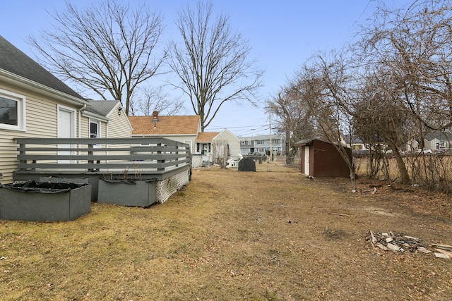 view of yard featuring an outdoor structure, a wooden deck, a storage shed, and fence