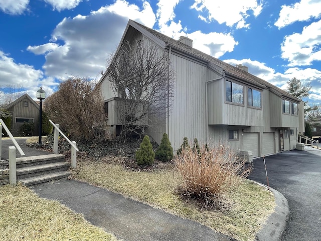 view of side of home featuring an attached garage, a chimney, and aphalt driveway