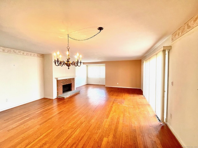 unfurnished living room with an inviting chandelier, light wood-style flooring, a fireplace, and baseboards