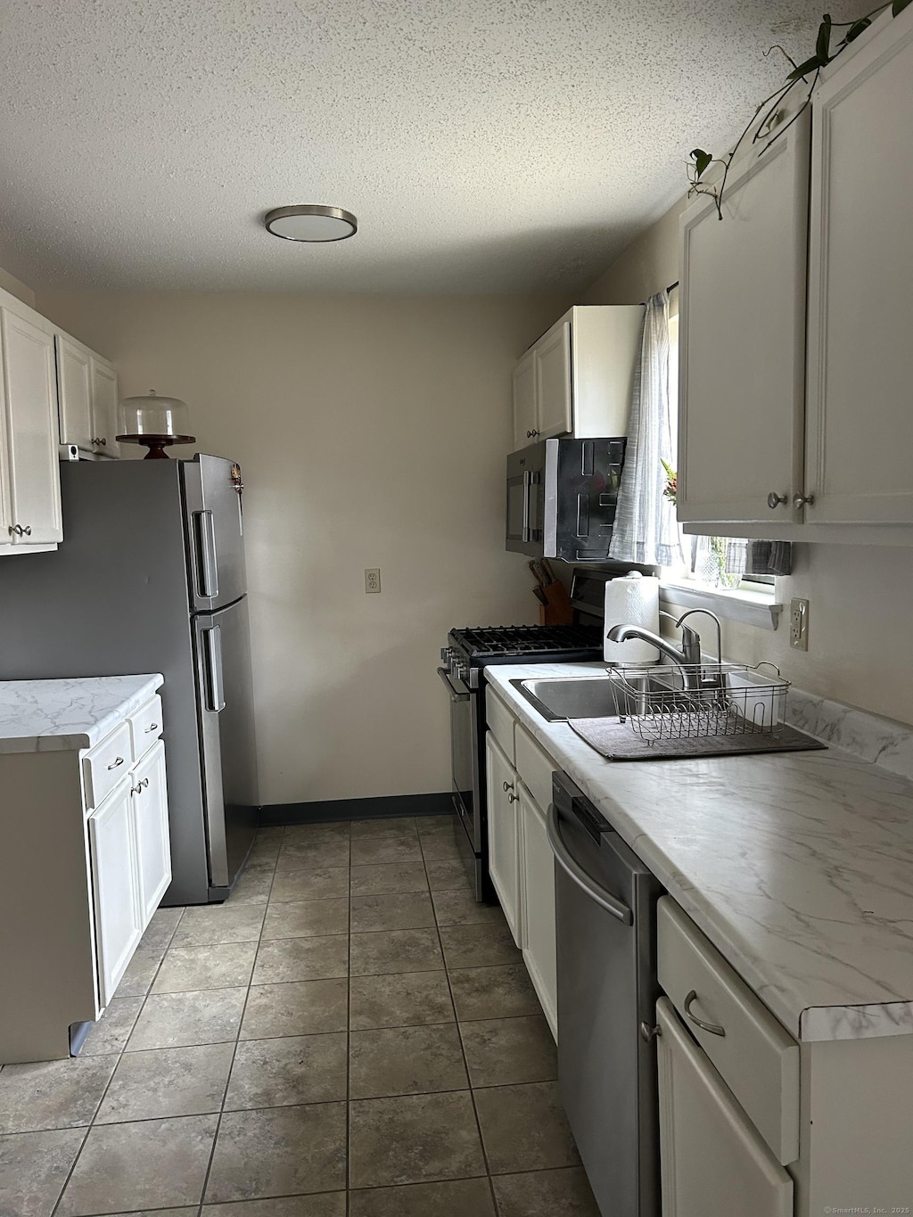 kitchen featuring tile patterned flooring, light countertops, appliances with stainless steel finishes, white cabinets, and a textured ceiling