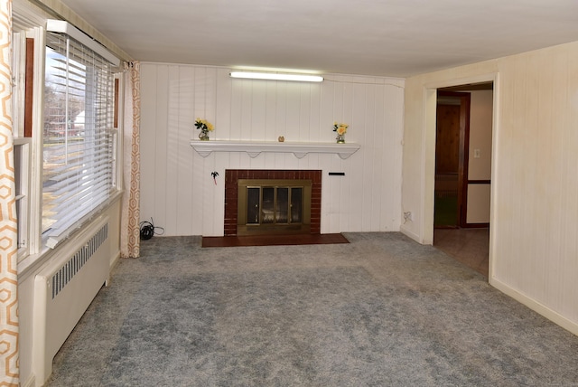 unfurnished living room featuring carpet floors, radiator heating unit, a brick fireplace, and baseboards