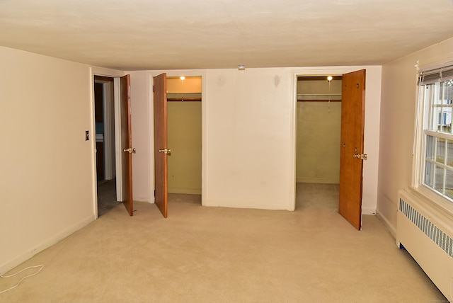 unfurnished bedroom featuring radiator heating unit, baseboards, multiple closets, and light colored carpet