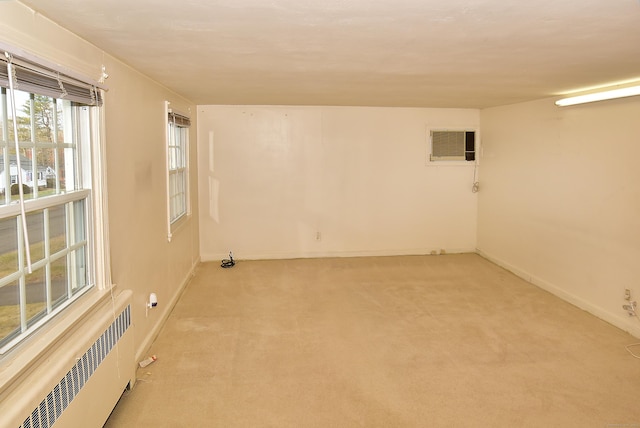 unfurnished room with radiator, light carpet, baseboards, and a wall mounted air conditioner