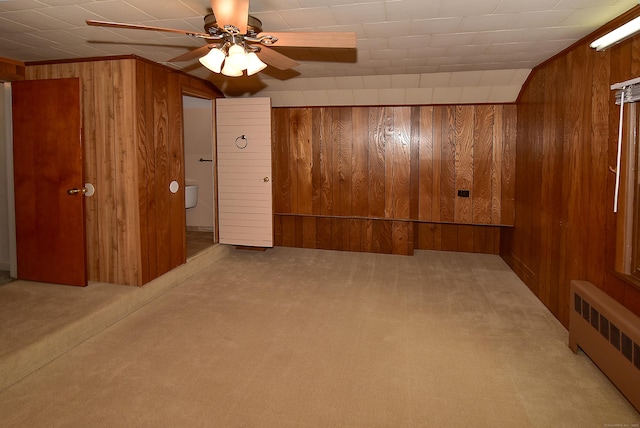 interior space featuring carpet floors, wood walls, radiator heating unit, and a ceiling fan