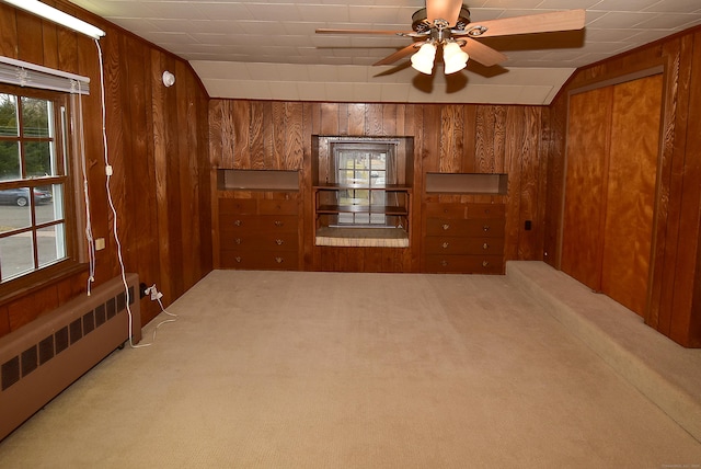 carpeted empty room featuring radiator heating unit, wooden walls, and a ceiling fan