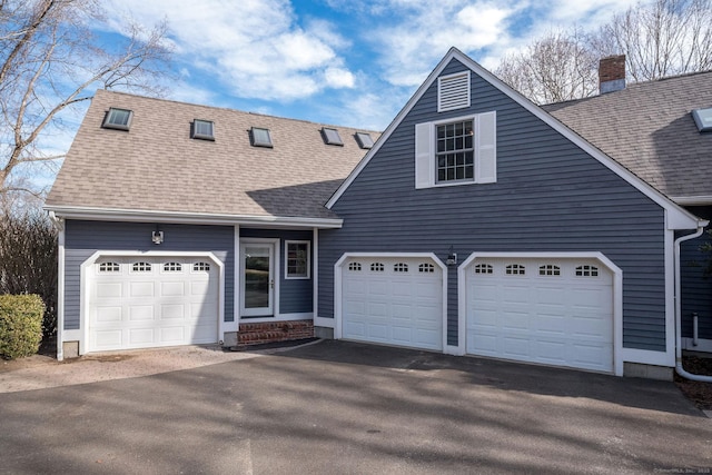 view of front of home featuring an attached garage, driveway, a chimney, and roof with shingles