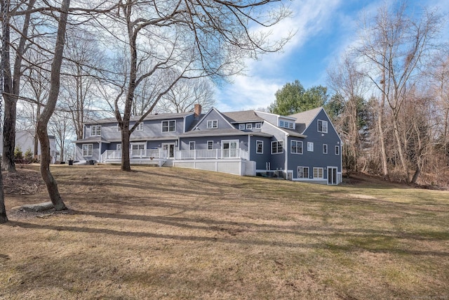 back of house featuring a wooden deck, a chimney, and a yard