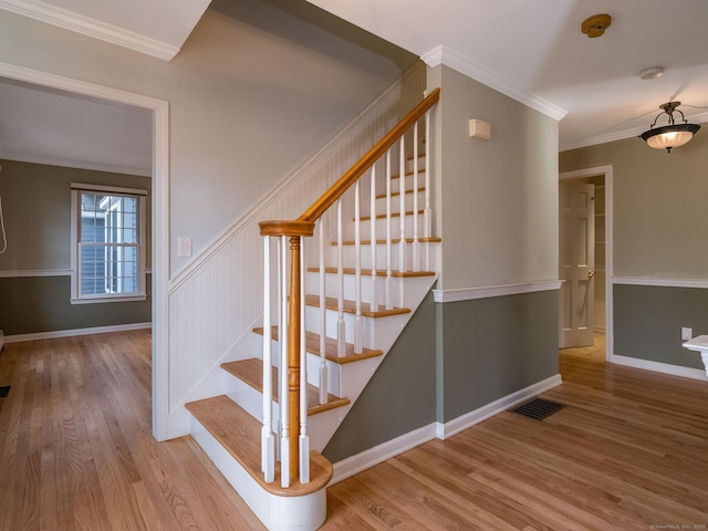 staircase featuring visible vents, a wainscoted wall, ornamental molding, wood finished floors, and baseboards