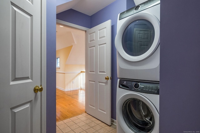 clothes washing area with laundry area, light tile patterned floors, baseboards, and stacked washer and clothes dryer