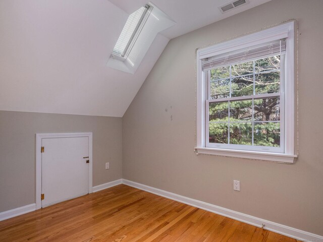 additional living space featuring visible vents, baseboards, light wood-style floors, and vaulted ceiling with skylight