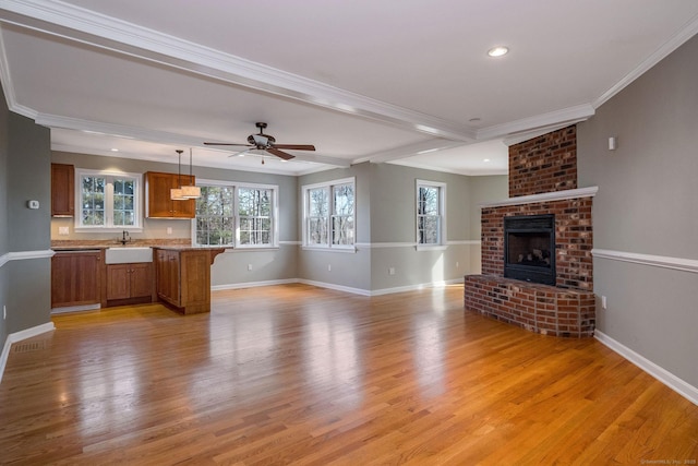 unfurnished living room with light wood finished floors, a brick fireplace, ceiling fan, baseboards, and ornamental molding