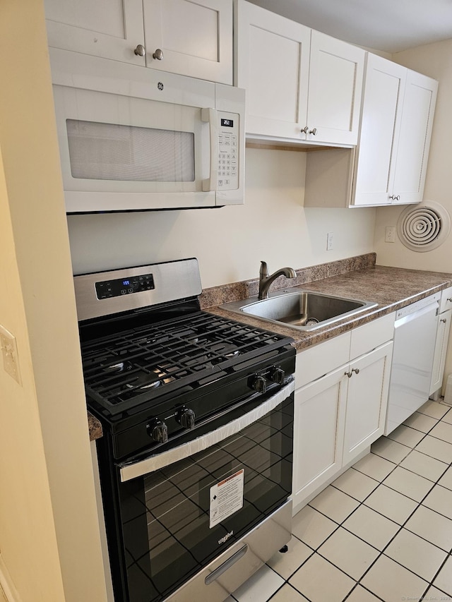 kitchen with light tile patterned floors, white cabinets, white appliances, and a sink