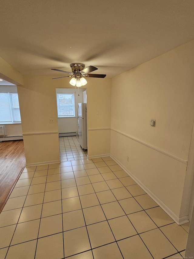 spare room featuring light tile patterned flooring, baseboards, a baseboard heating unit, and a ceiling fan