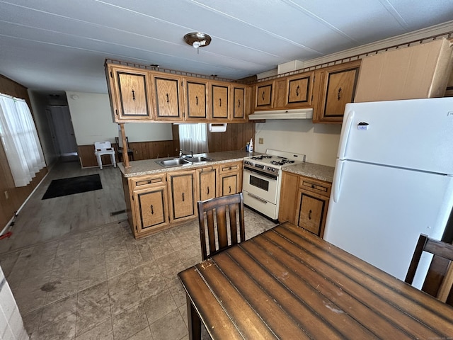 kitchen featuring under cabinet range hood, white appliances, brown cabinetry, and a sink