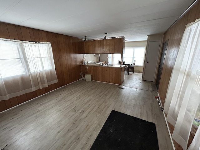 kitchen featuring brown cabinets, light wood-style flooring, open floor plan, a peninsula, and wood walls