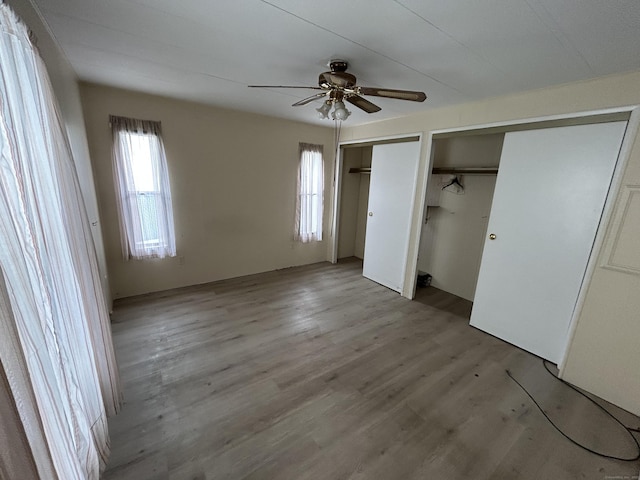 unfurnished bedroom with light wood-style flooring, two closets, and ceiling fan