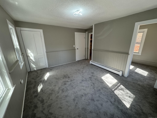 unfurnished bedroom with carpet floors, baseboard heating, a textured ceiling, and wainscoting