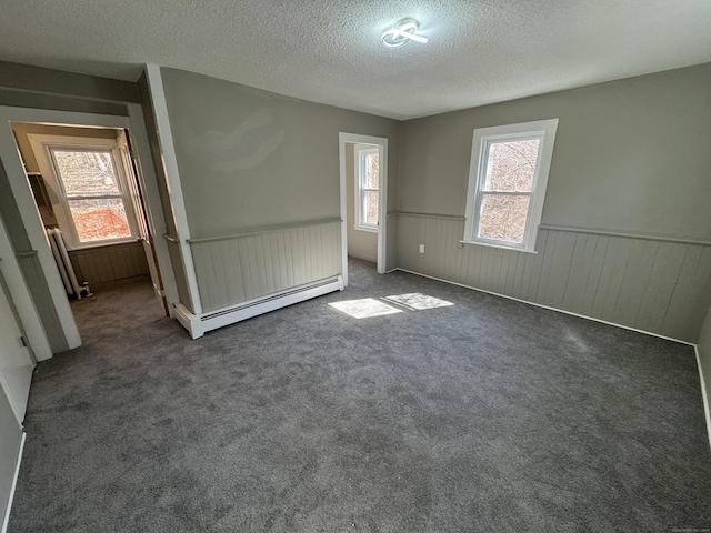 unfurnished bedroom with a wainscoted wall, a baseboard radiator, carpet, and a textured ceiling