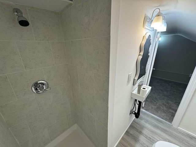 full bath featuring lofted ceiling, a tile shower, and wood finished floors