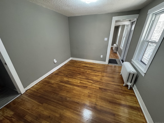 empty room featuring radiator heating unit, baseboards, and wood finished floors