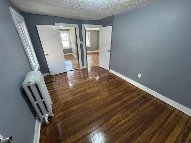 spare room with radiator, a textured ceiling, baseboards, and wood finished floors