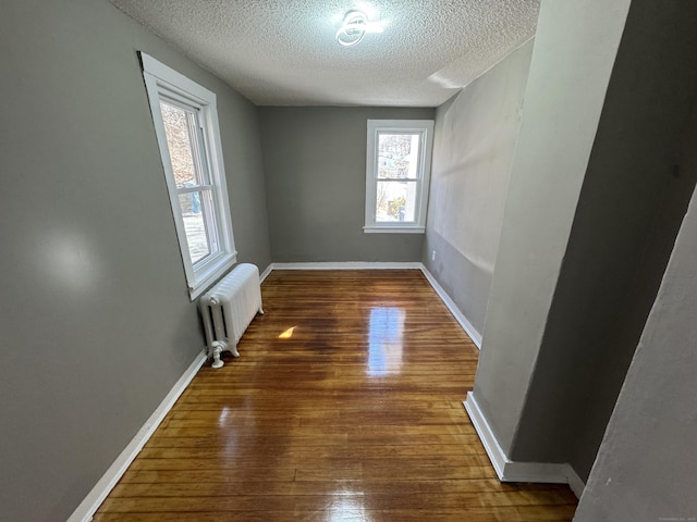 spare room featuring radiator, a textured ceiling, baseboards, and wood finished floors