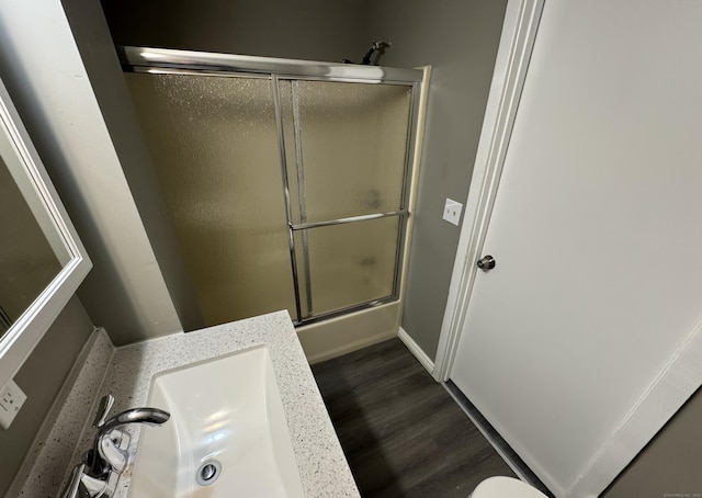 full bathroom with baseboards, combined bath / shower with glass door, a sink, and wood finished floors