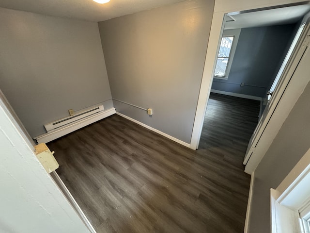 empty room with a baseboard heating unit, dark wood-style floors, and baseboards