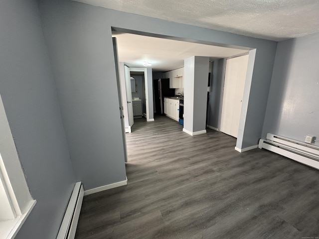 spare room featuring baseboard heating, baseboards, dark wood finished floors, and a textured ceiling