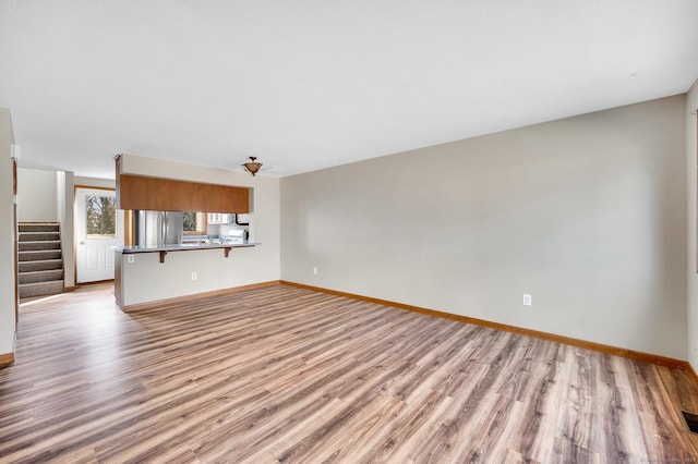 unfurnished living room featuring light wood-type flooring, baseboards, and stairway