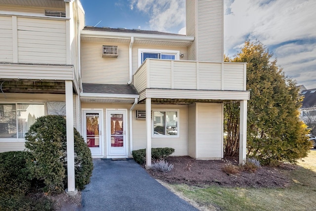 doorway to property with a balcony, a chimney, and a shingled roof