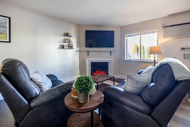 living room featuring a glass covered fireplace, baseboards, wood finished floors, and a wall unit AC