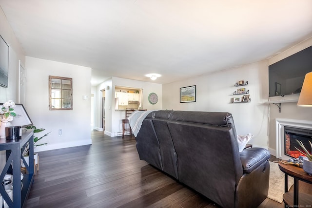 living room featuring a glass covered fireplace, baseboards, and dark wood finished floors