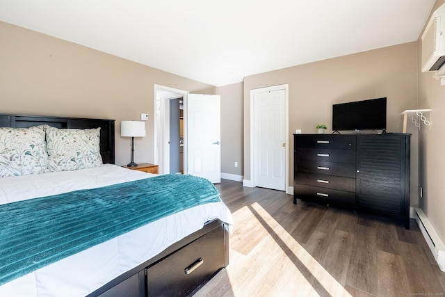 bedroom with baseboards, baseboard heating, an AC wall unit, and wood finished floors