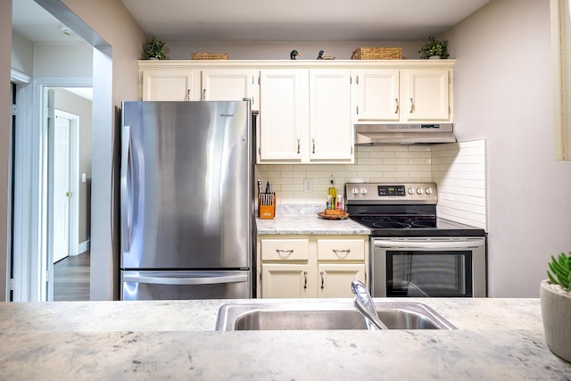 kitchen with tasteful backsplash, under cabinet range hood, appliances with stainless steel finishes, white cabinetry, and a sink