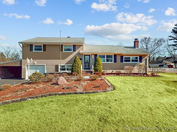 split level home featuring an attached garage, a chimney, a front yard, and fence