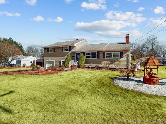 back of property with a lawn, a chimney, and an attached garage