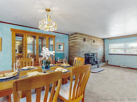 dining room with visible vents, a notable chandelier, carpet flooring, baseboards, and a wood stove