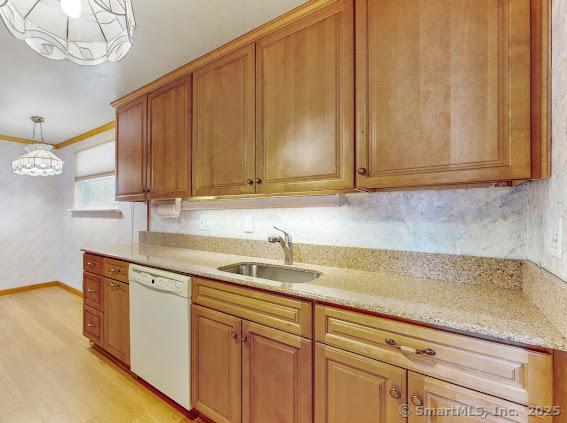 kitchen with decorative light fixtures, dishwasher, light wood-type flooring, brown cabinetry, and a sink