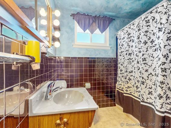 bathroom with a wainscoted wall, a sink, curtained shower, tile walls, and tile patterned flooring