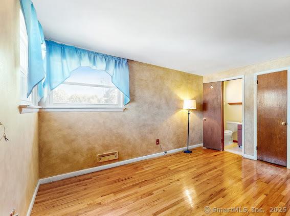 unfurnished bedroom with visible vents, multiple closets, wood finished floors, connected bathroom, and baseboards