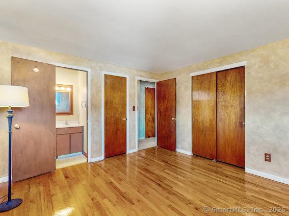 unfurnished bedroom with baseboards, two closets, ensuite bath, and wood finished floors