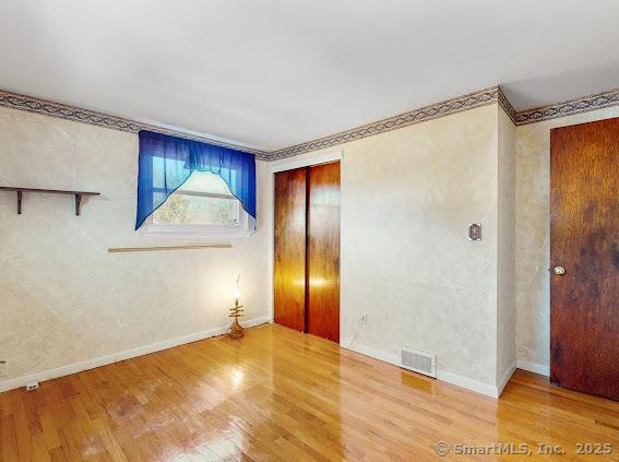 unfurnished room featuring wood finished floors, visible vents, a textured wall, and baseboards