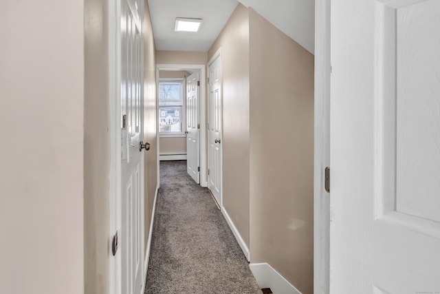 hallway featuring baseboards, dark colored carpet, and a baseboard radiator