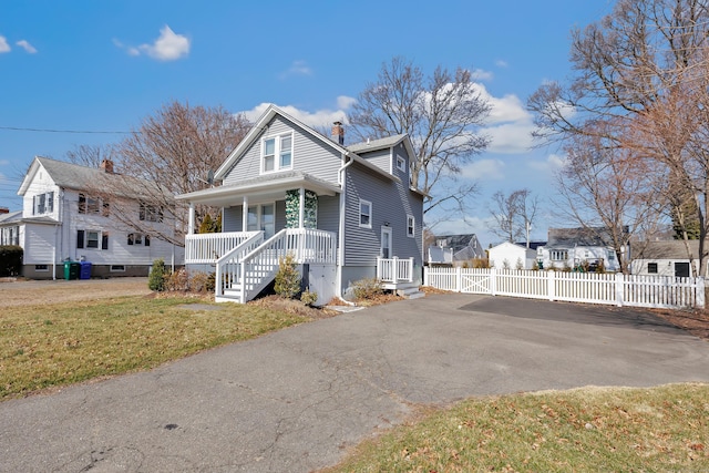 view of front of house with aphalt driveway, fence, covered porch, a front yard, and a chimney