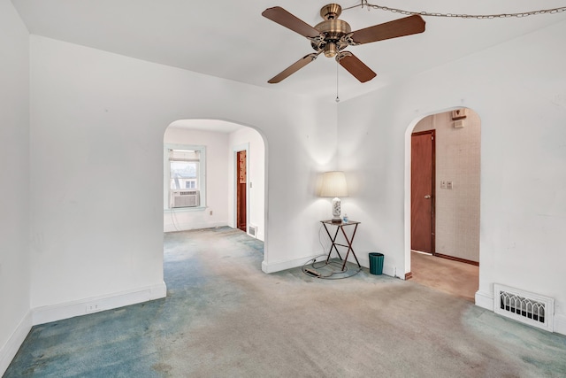 carpeted empty room with visible vents, baseboards, cooling unit, arched walkways, and a ceiling fan