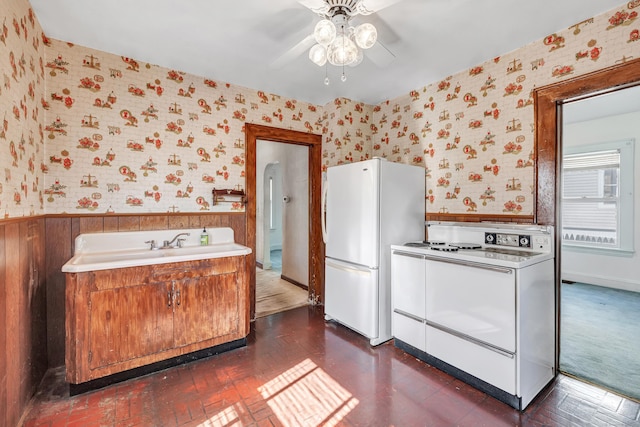 kitchen with a wainscoted wall, brown cabinets, washer / clothes dryer, white appliances, and wallpapered walls