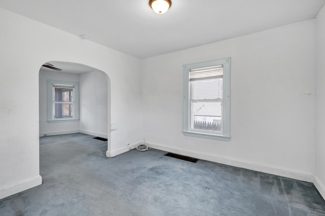 empty room with carpet, visible vents, arched walkways, and baseboards