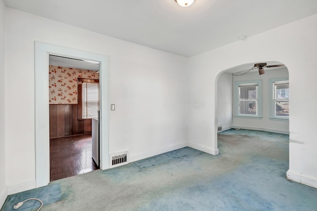 empty room with wooden walls, carpet, visible vents, arched walkways, and ceiling fan