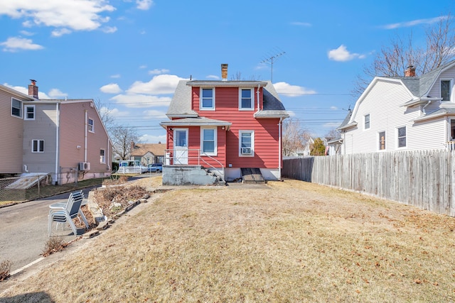 back of house with a yard, a shingled roof, a chimney, and fence